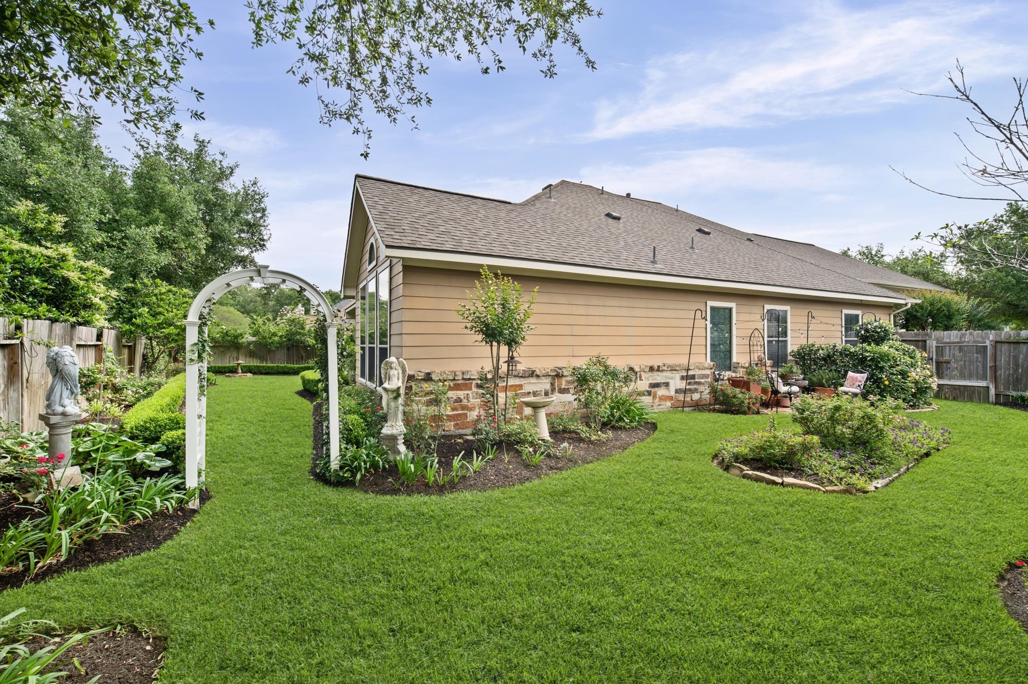 1603 Claytons Bend Court Spring, TX 77386 - Photo 29 of 38 Charming home with a beautifully landscaped backyard featuring lush green grass, a white garden arch, and well-maintained flower beds. The exterior is a combination of siding and stone, offering a cozy and inviting atmosphere. Perfect for enjoying outdoor activities and gardening.