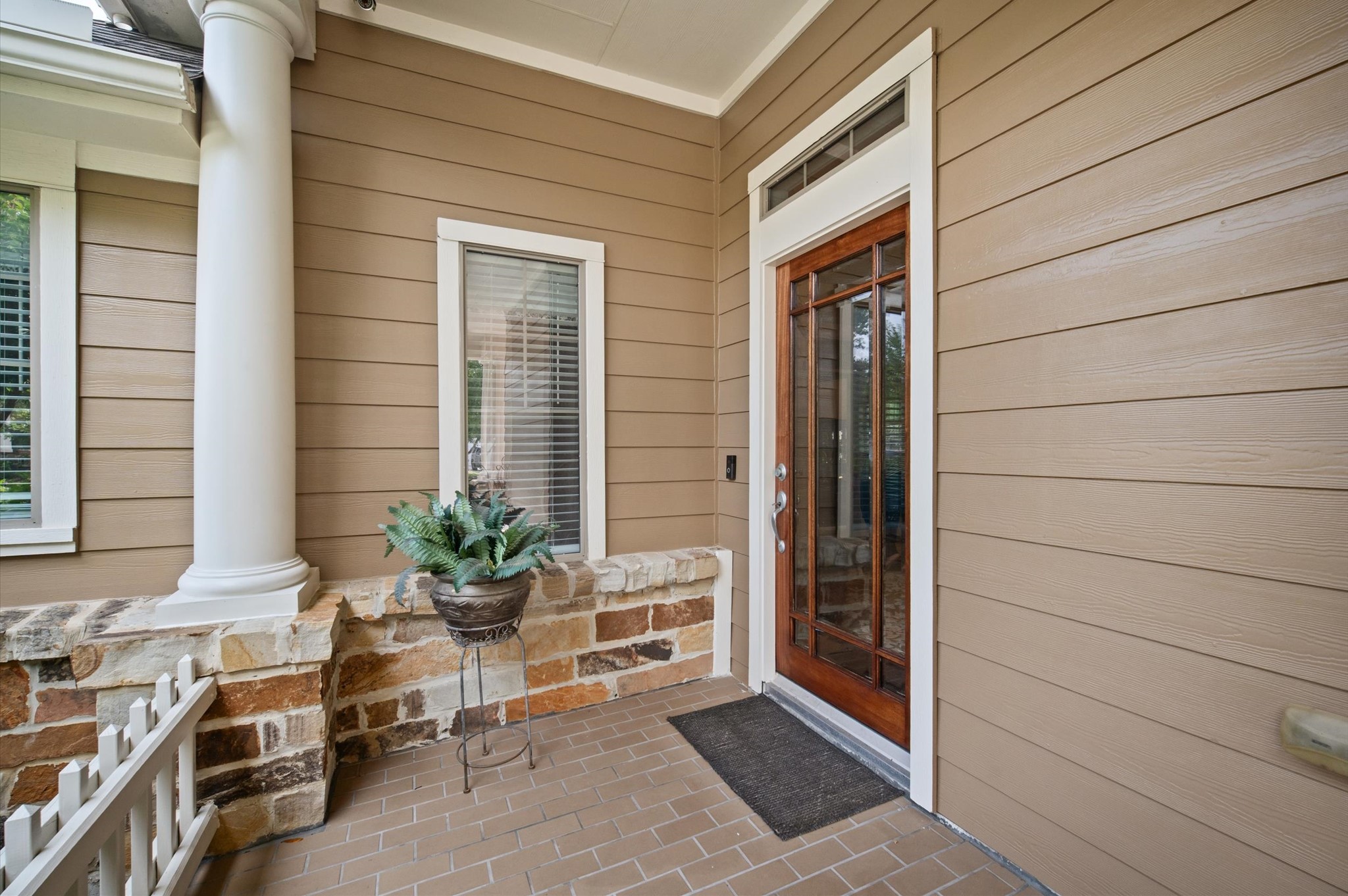 1603 Claytons Bend Court Spring, TX 77386 - Photo 34 of 38 Charming front porch with a wooden door featuring glass panels, complemented by beige siding and a stone accent wall. A classic column and a potted plant add elegance and warmth to the entrance.
