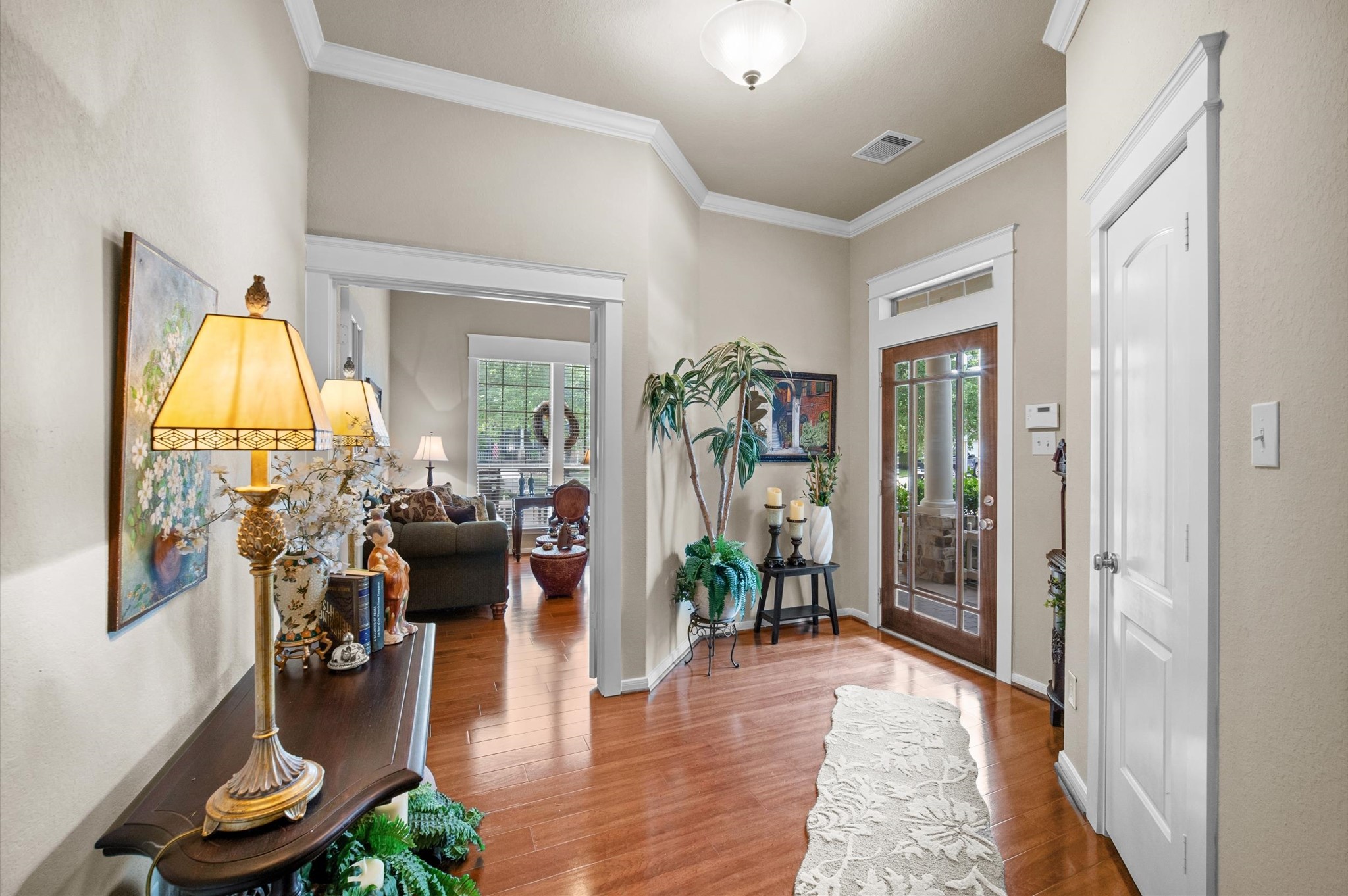 1603 Claytons Bend Court Spring, TX 77386 - Photo 6 of 38 This inviting entryway features warm wood flooring and elegant crown molding. It leads into a cozy living area with natural light streaming through large windows. Decor includes tasteful artwork and greenery, creating a welcoming ambiance.
