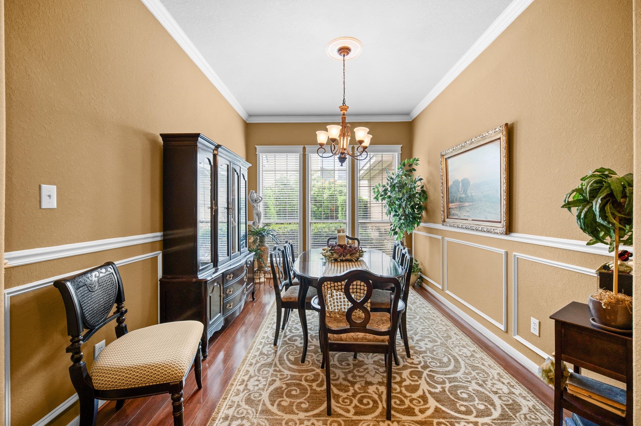 1603 Claytons Bend Court Spring, TX 77386 - Photo 8 of 38 A beautifully decorated dining room featuring warm-toned walls, elegant crown molding, and a classic chandelier. It includes a large window for natural light, a dark wood dining set, and a matching china cabinet. The room is accented with plants and artwork, creating an inviting atmosphere.