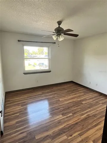 an empty room with wooden floor fan and windows