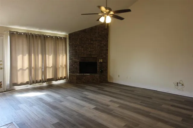 an empty room with wooden floor chandelier fan and windows