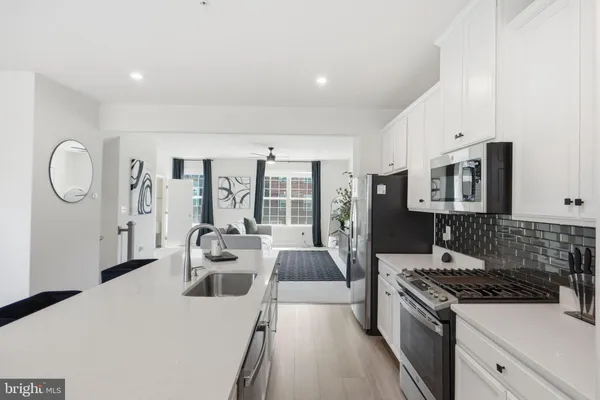 a kitchen with stainless steel appliances granite countertop a stove a sink dishwasher and white cabinets with wooden floor