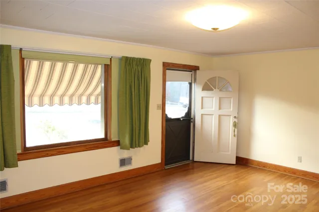 a view of an empty room with wooden floor and a window