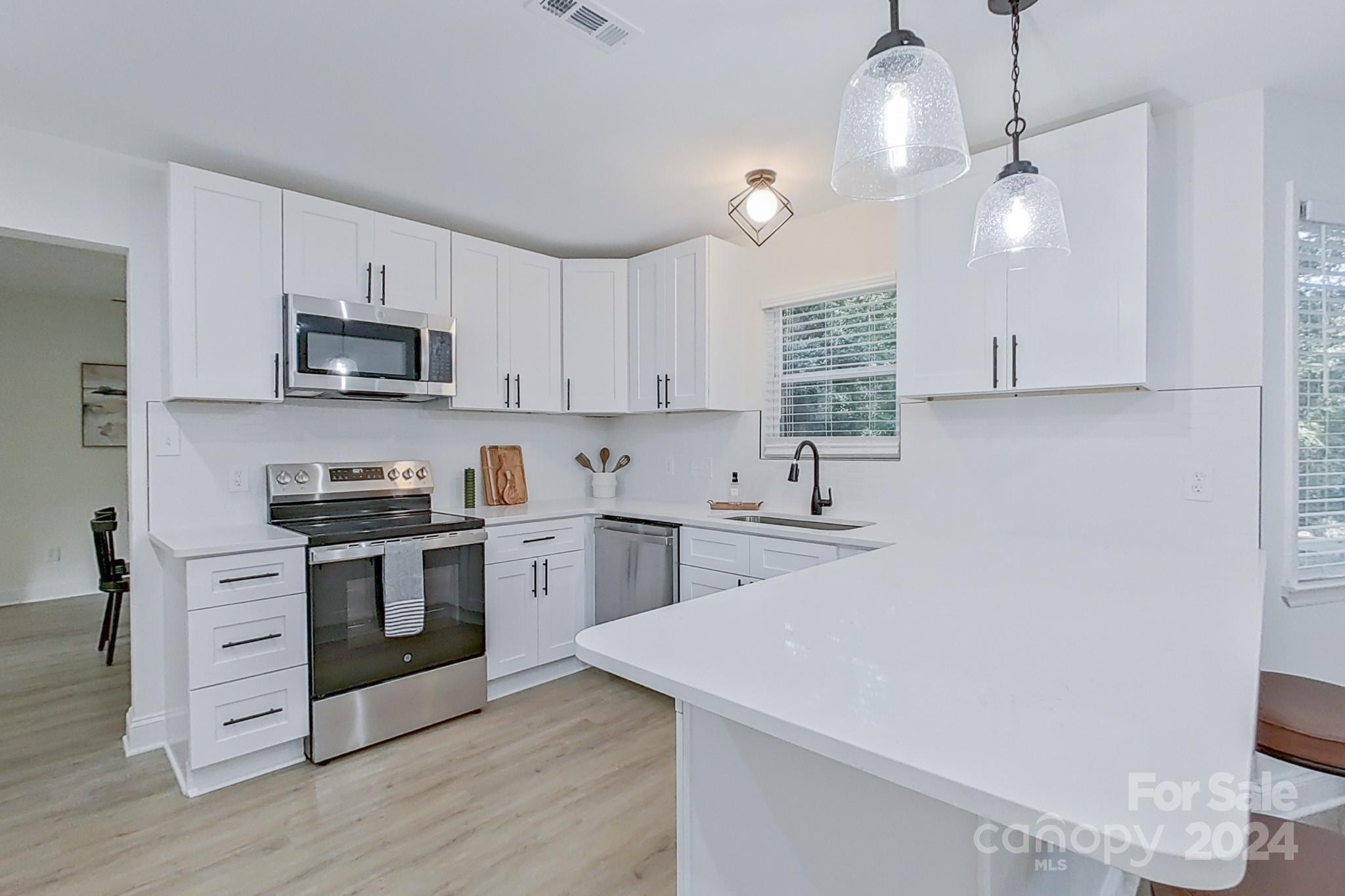 5710 Stream Ridge Drive Charlotte, NC 28269 - Photo 19 of 48 a kitchen with stainless steel appliances white cabinets a sink a stove a microwave and wooden floors