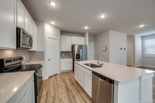 a kitchen that has a sink a refrigerator and a stove top oven with wooden floor
