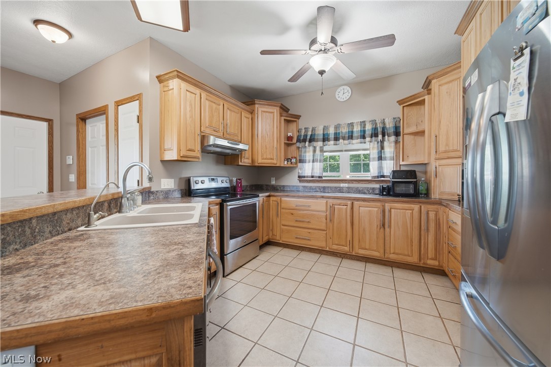 12159 Lawndell Road Southwest Beach City, OH 44608 - Photo 14 of 49 Kitchen featuring wood cabinetry, laminate countertops, a double basin sink with a gooseneck faucet, stainless steel appliances, and tile flooring
