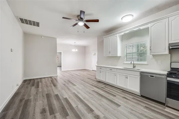 a kitchen with granite countertop a stove a sink and white cabinets with wooden floor