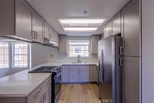 a kitchen with stainless steel appliances granite countertop a refrigerator a sink dishwasher a stove and white countertops with wooden floor