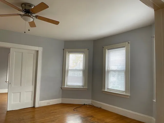 an empty room with wooden floor fan and windows