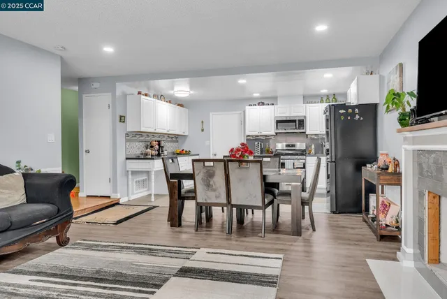 a kitchen with stainless steel appliances kitchen island granite countertop a refrigerator a stove a microwave oven a dining table and chairs with wooden floor