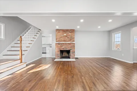 an empty room with wooden floor fireplace and windows