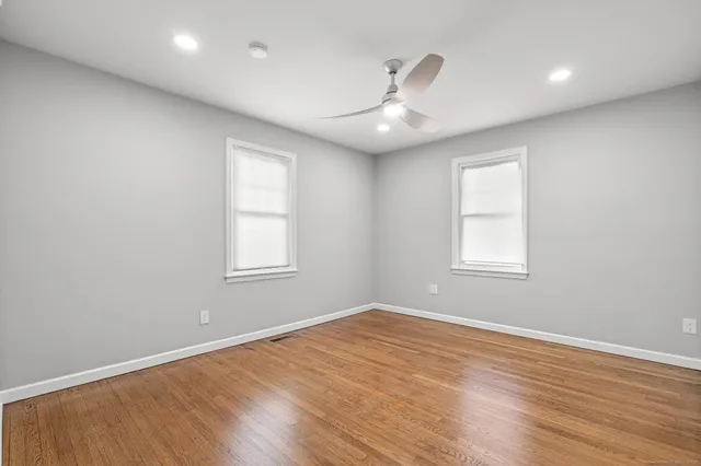 an empty room with wooden floor ceiling fan and windows