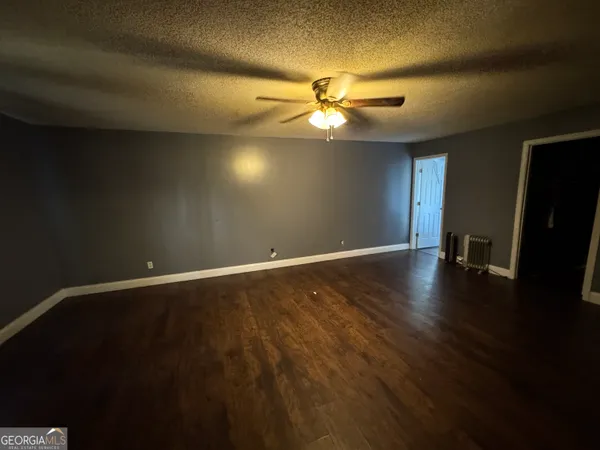 a view of an empty room with wooden floor and a ceiling fan