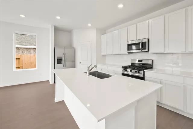 a kitchen with stainless steel appliances a sink a stove a microwave a refrigerator a white cabinets and wooden floor