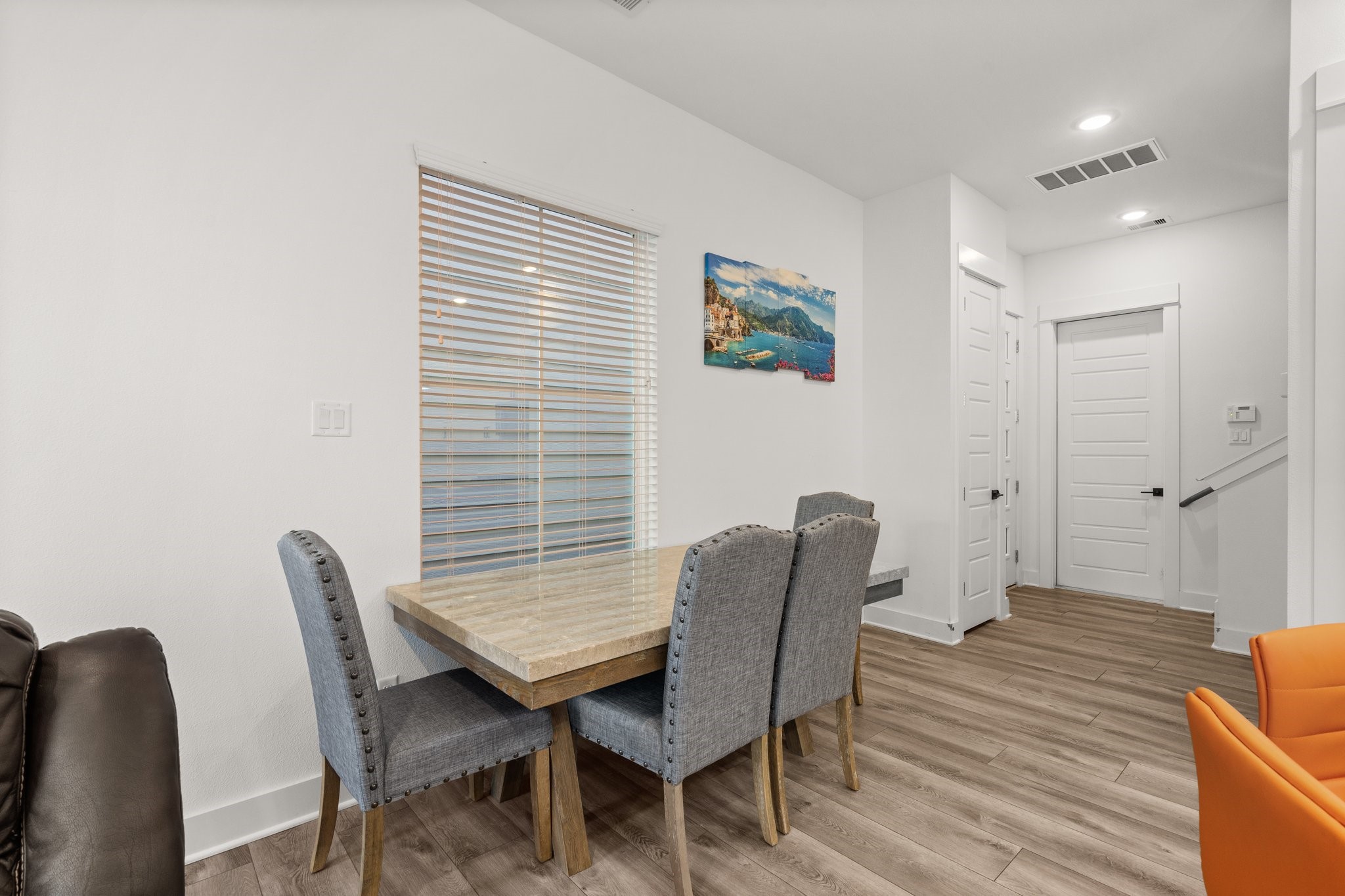 2928 Stevens Street Houston, TX 77026 - Photo 7 of 30 This photo showcases a modern dining area with a wooden table and upholstered chairs, set against light-colored walls. The space features wood flooring, a window with blinds, and a hallway with doors, creating a cozy and functional living area.