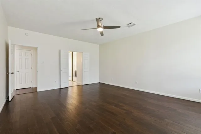a view of an empty room with wooden floor and a ceiling fan