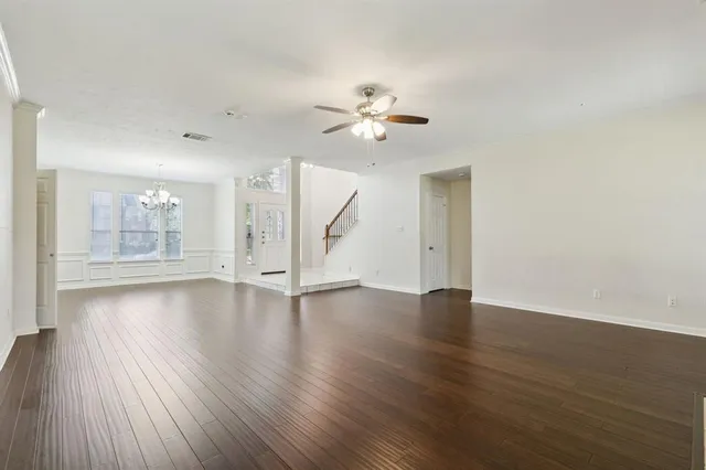 a view of an empty room with wooden floor and a ceiling fan