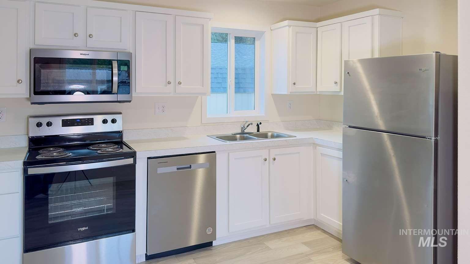 10 Kamloop Lane Orofino, ID 83544 - Photo 4 of 17 Kitchen featuring white cabinetry, stainless steel appliances, a double basin sink with a chrome faucet, light-toned countertops, and wood-finish flooring
