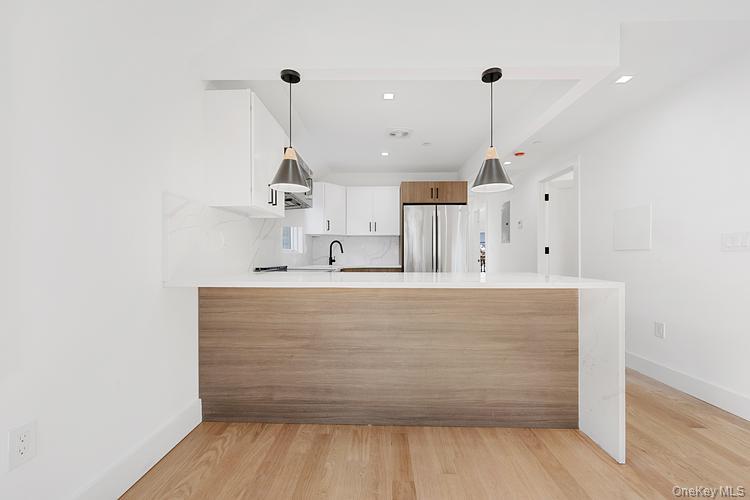 38-40 215th Street Queens, NY 11361 - Photo 17 of 35 Kitchen featuring a peninsula, decorative light fixtures, light wood-style floors, freestanding refrigerator, and recessed lighting