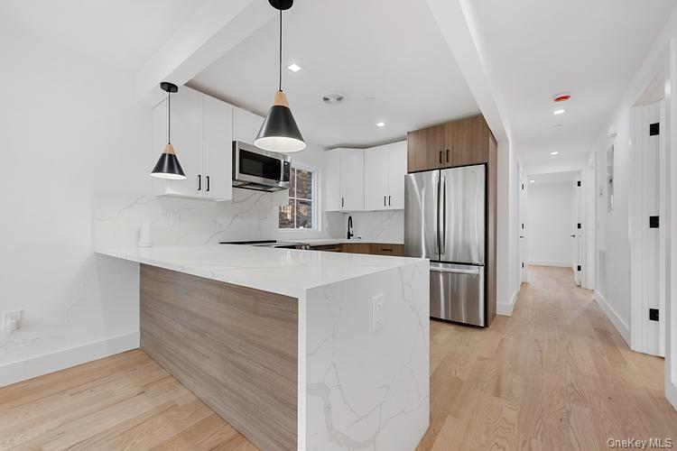 38-40 215th Street Queens, NY 11361 - Photo 24 of 35 Kitchen with decorative backsplash, appliances with stainless steel finishes, decorative light fixtures, light stone counters, and light wood-style floors