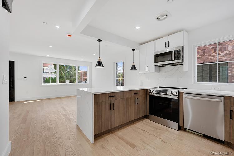 38-40 215th Street Queens, NY 11361 - Photo 25 of 35 Kitchen with appliances with stainless steel finishes, light wood-style flooring, pendant lighting, light stone countertops, and white cabinets
