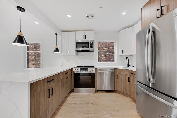 38-40 215th Street Queens, NY 11361 - Photo 26 of 35 Kitchen with stainless steel appliances, brown cabinetry, decorative light fixtures, light wood-type flooring, and light stone counters