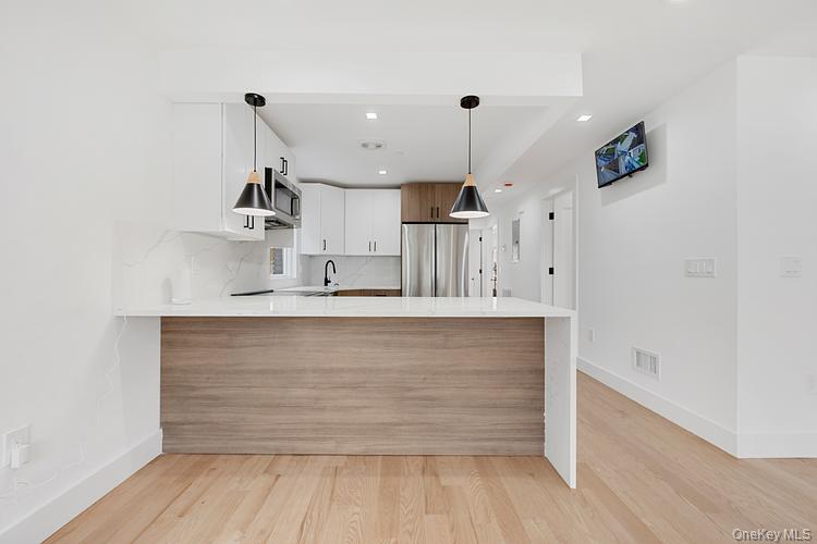 38-40 215th Street Queens, NY 11361 - Photo 29 of 35 Kitchen with a peninsula, decorative backsplash, hanging light fixtures, light wood-style flooring, and appliances with stainless steel finishes