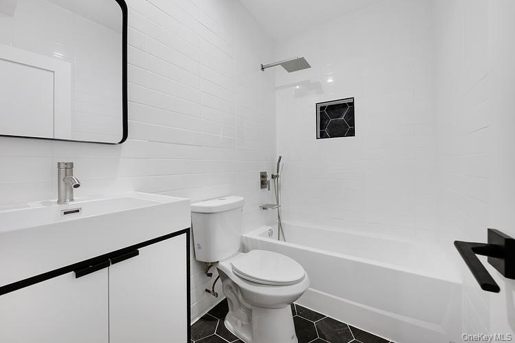 38-40 215th Street Queens, NY 11361 - Photo 31 of 35 Bathroom featuring vanity, tub / shower combination, dark tile patterned flooring, and tile walls