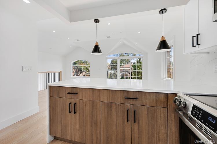 38-40 215th Street Queens, NY 11361 - Photo 7 of 35 Kitchen with stainless steel range with electric stovetop, hanging light fixtures, light wood-style floors, brown cabinets, and lofted ceiling