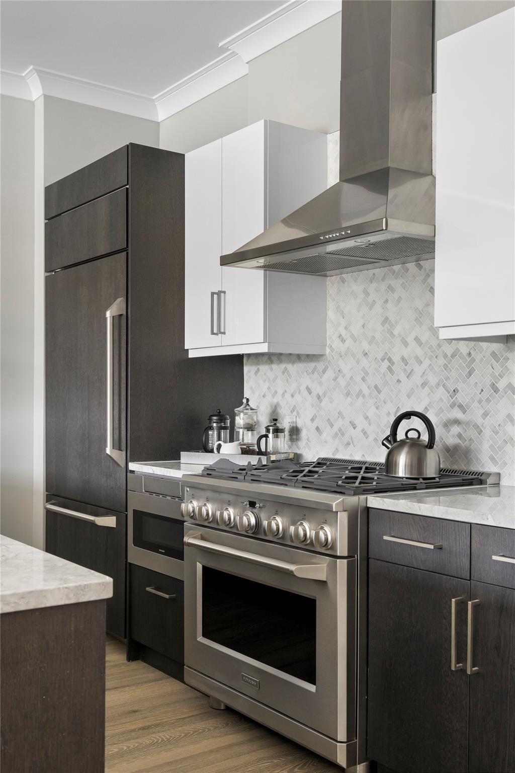 100 Garvies Point Road, Unit 1211 Glen Cove, NY 11542 - Photo 5 of 24 Kitchen with crown molding, backsplash, premium appliances, white cabinets, and wall chimney exhaust hood