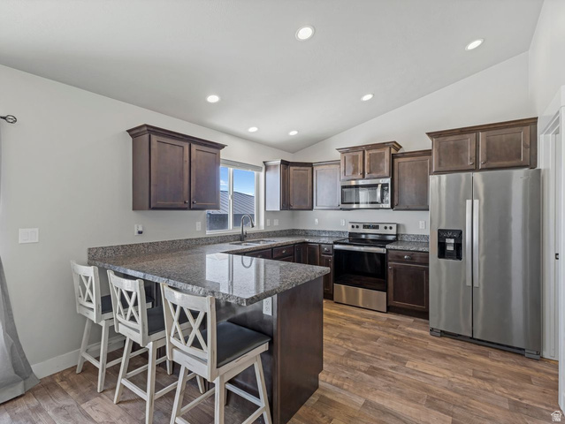573 South Maxwell Drive Grantsville, UT 84029 - Photo 8 of 25 Kitchen featuring stainless steel appliances, dark wood finish cabinets, a kitchen bar, a peninsula, and dark stone countertops