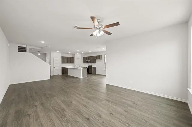 an empty room with wooden floor ceiling fan and windows