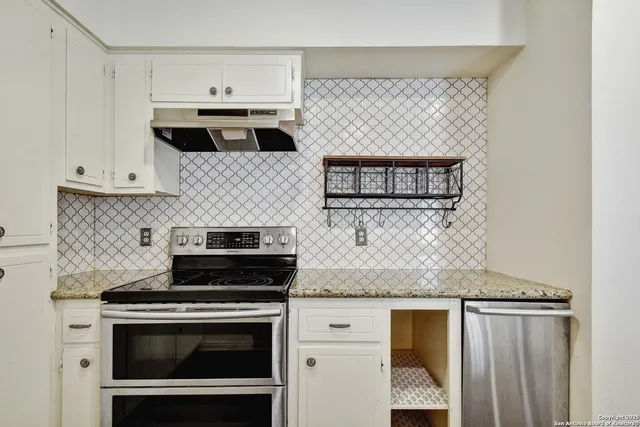 a kitchen with granite countertop a stove oven and white cabinets
