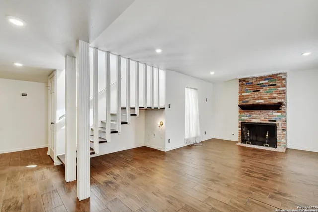 an empty room with wooden floor fireplace and windows
