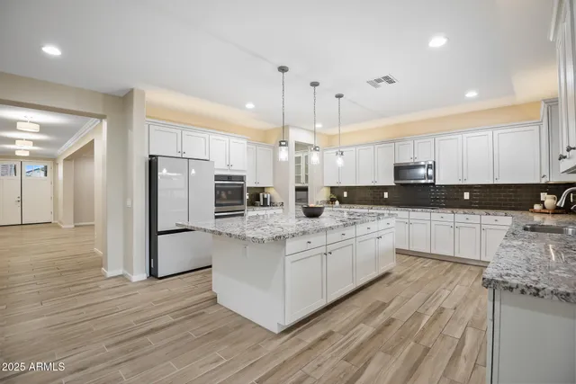 a large kitchen with stainless steel appliances a refrigerator a sink dishwasher a oven and white cabinets with wooden floor