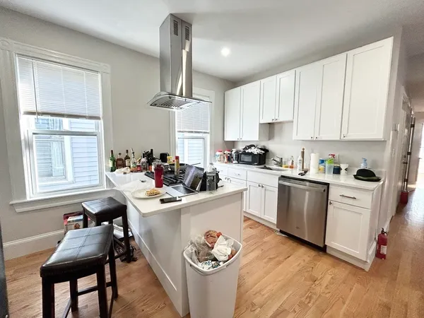 a kitchen with stainless steel appliances kitchen island granite countertop a sink dishwasher a stove and white cabinets with wooden floor