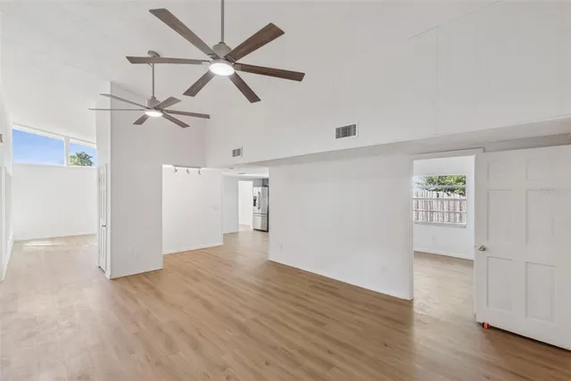 an empty room with wooden floor ceiling fan and windows