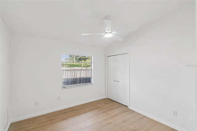 an empty room with wooden floor ceiling fan and windows