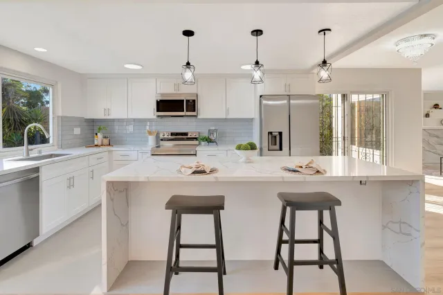 a kitchen with stainless steel appliances a sink a stove a refrigerator cabinets and a dining table with wooden floor