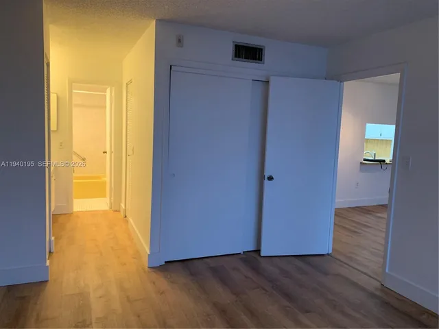 a view of an empty room with wooden floor and a bathroom