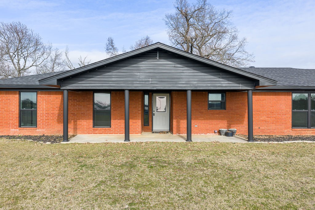 Front of  house featuring a porch, a lawn, and brick siding