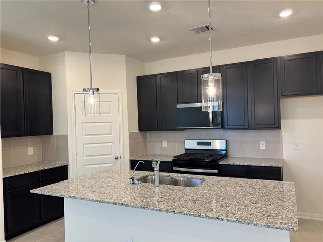 a kitchen with kitchen island granite countertop stainless steel appliances a refrigerator a stove a sink and cabinets