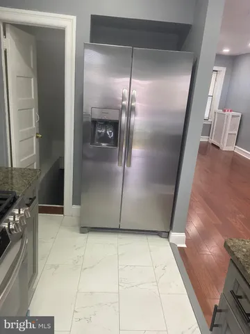a view of a refrigerator in kitchen and an empty room with wooden floor