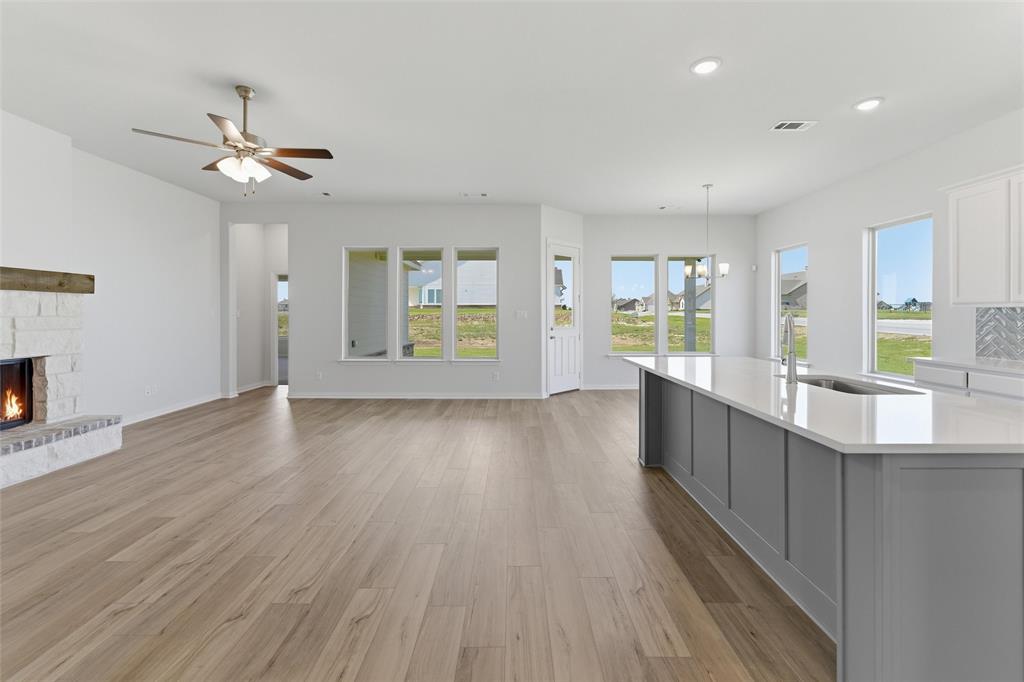 104 Snowy Owl Trail Rhome, TX 76078 - Photo 10 of 27 Open concept living space featuring wood-finish flooring, a white brick fireplace with a wood mantle, and an expansive kitchen island with a light-colored countertop