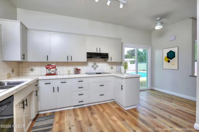 a kitchen with granite countertop white cabinets white appliances a sink and a wooden floor