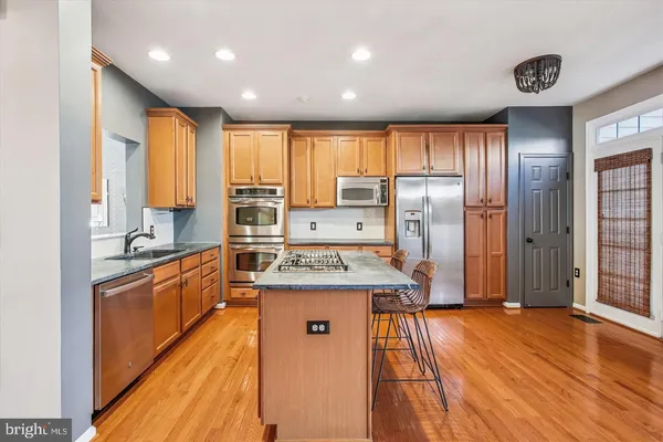 a kitchen with stainless steel appliances granite countertop a refrigerator a sink dishwasher a stove and white countertops with wooden floor