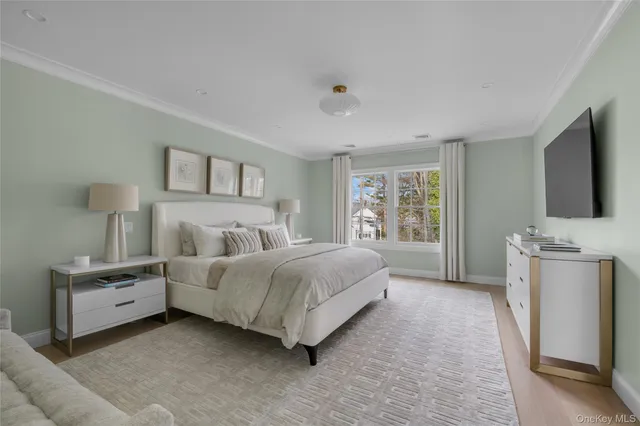 a spacious bedroom with a bed and a flat tv screen on the dresser