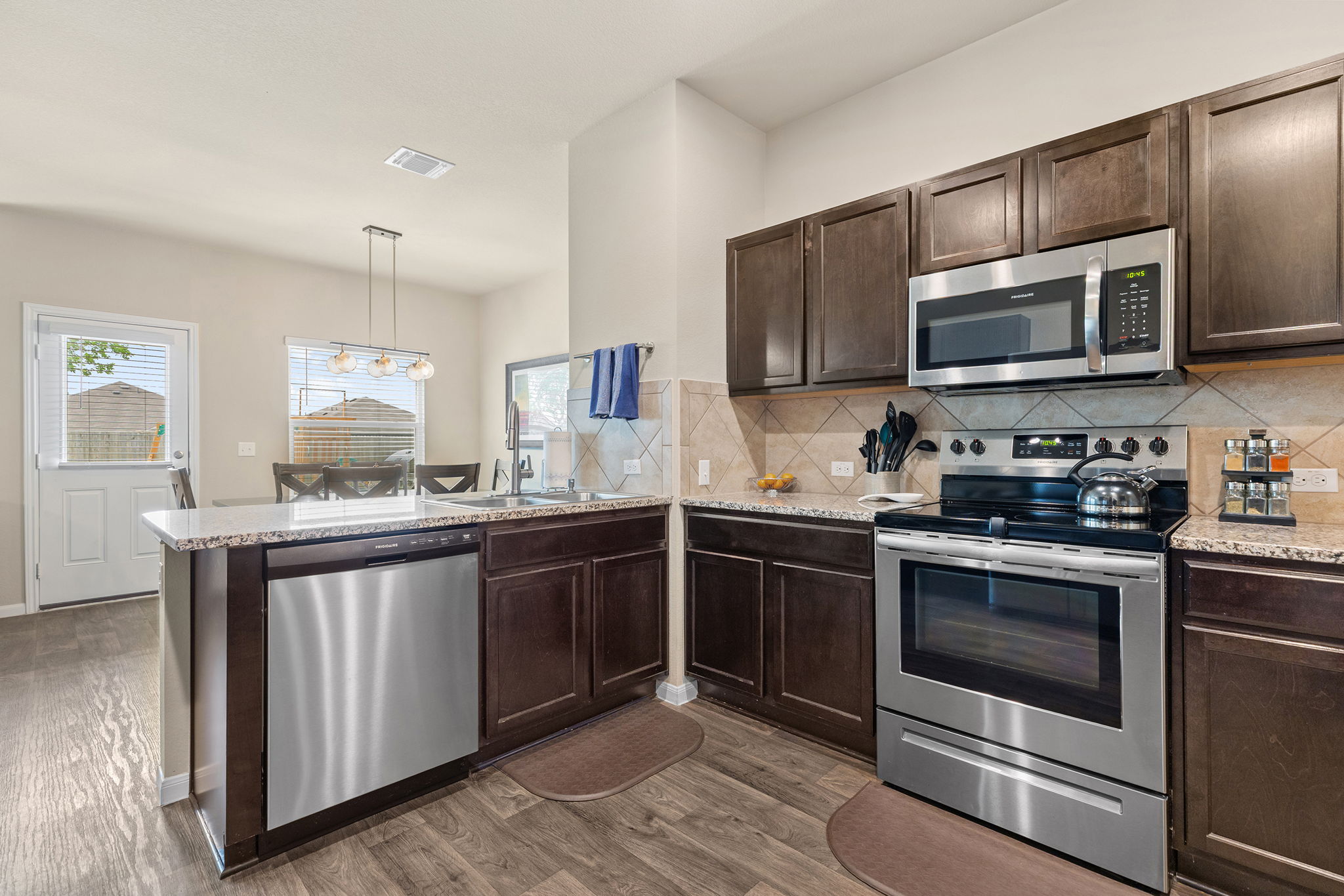 404 Cassandra Drive Hutto, TX 78634 - Photo 9 of 40 Kitchen with stainless steel appliances, dark wood finish cabinetry, a peninsula, backsplash, and light stone counters