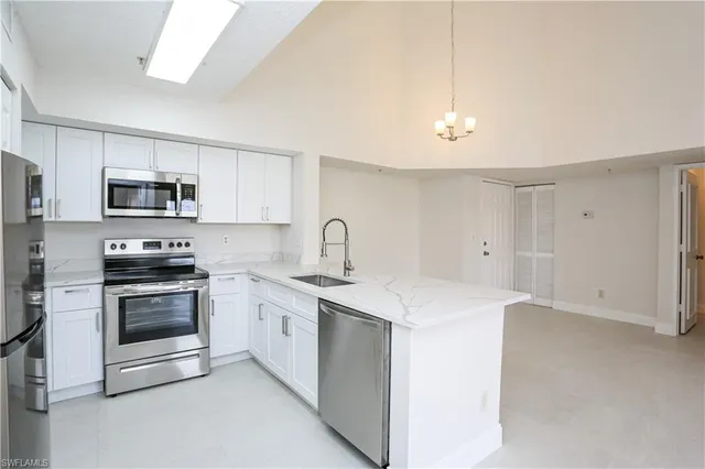 a white kitchen with stainless steel appliances granite countertop a sink a stove a microwave and a refrigerator